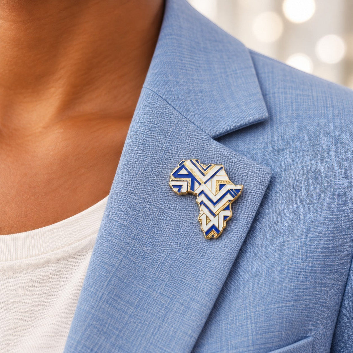 Broche Renaissance Ébène Likolo en forme de carte d'Afrique, émaillée bleu, blanc et doré sur un blazer bleu clair.