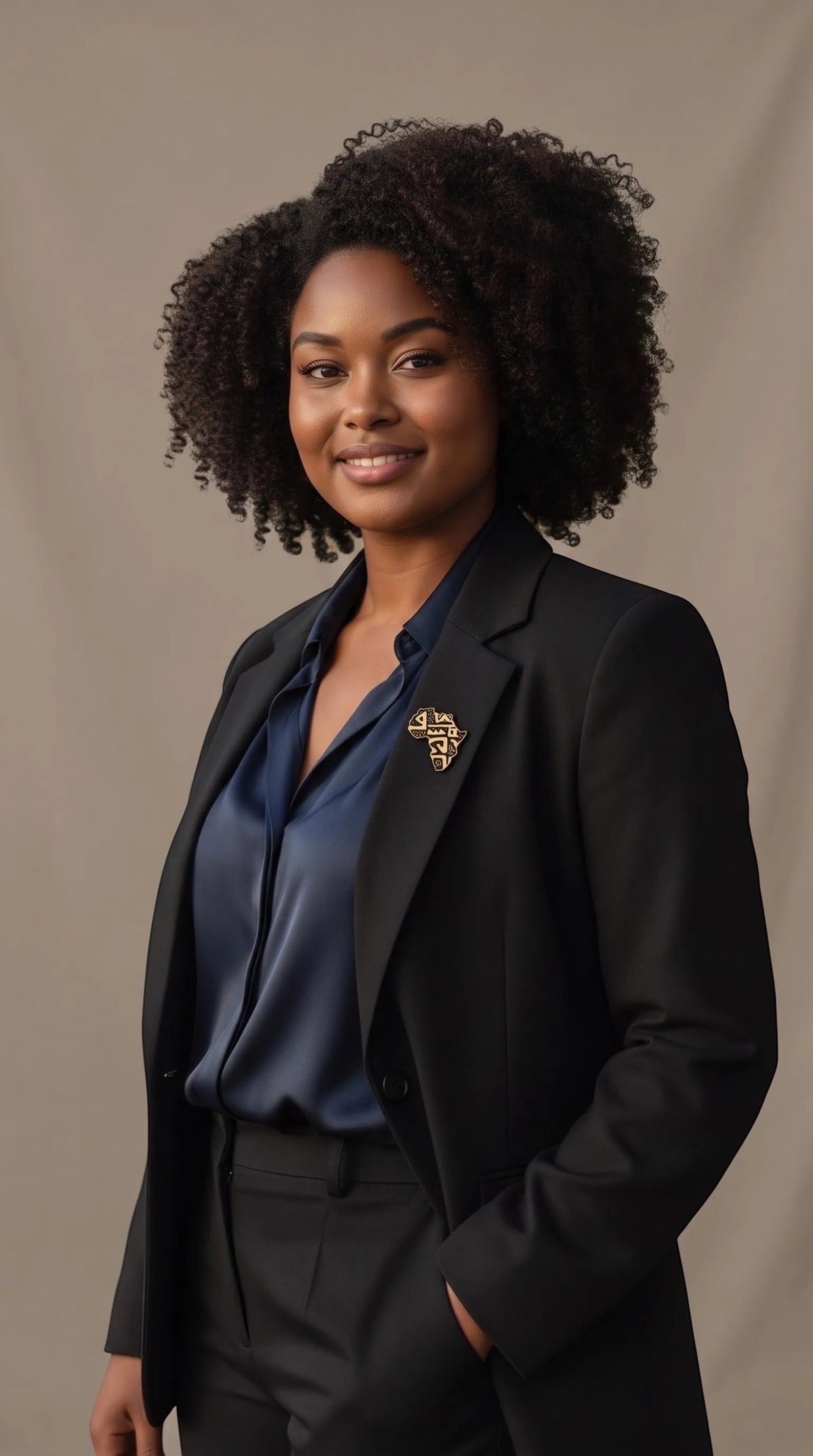 Femme portant la broche dorée Sankofa de Renaissance Ébène en forme de carte d'Afrique sur un blazer noir élégant